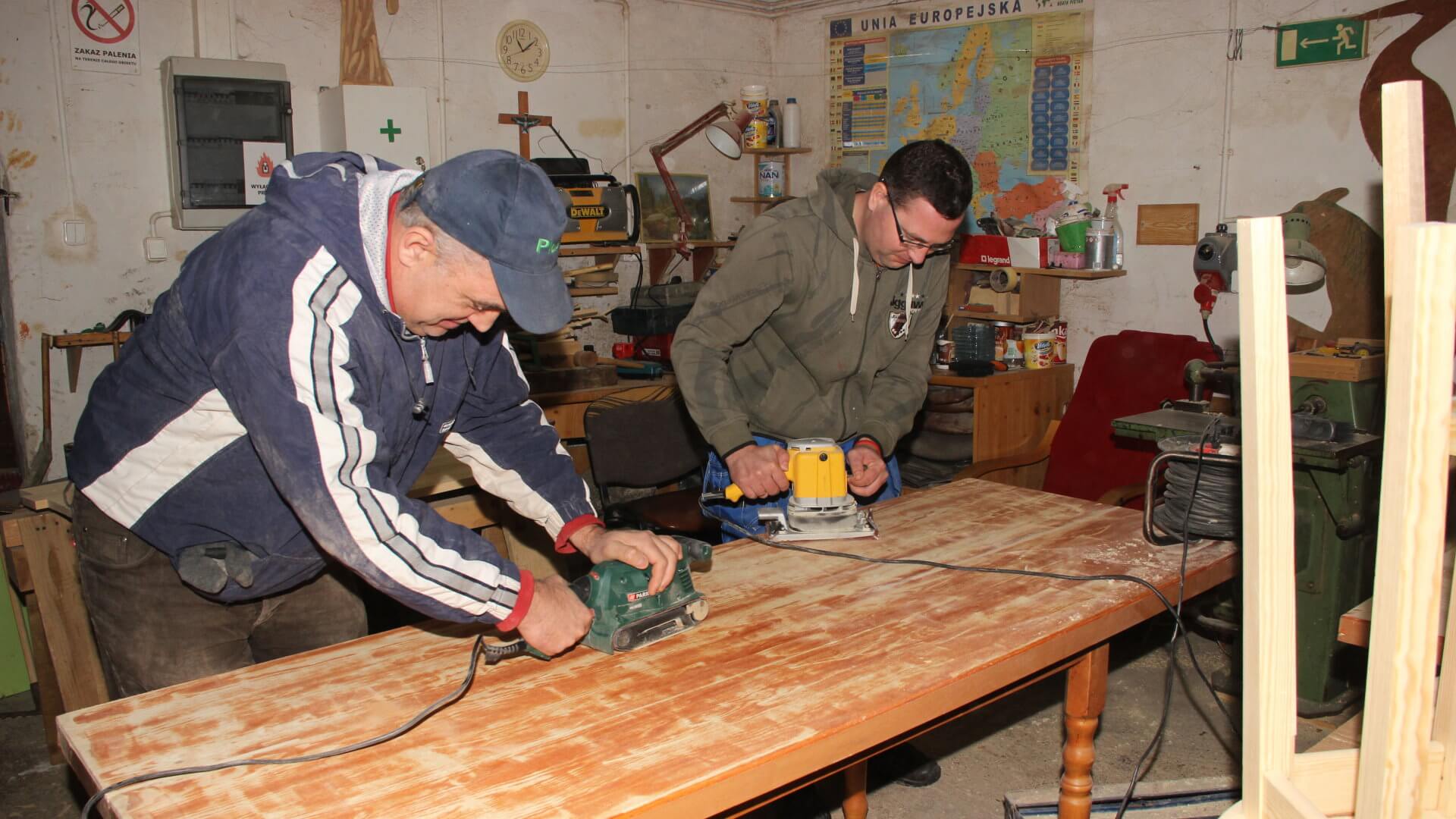Uczestnicy Warsztatu Terapii Zajęciowej w Kwidzynie szlifują stół w pracowni edukacyjno-stolarskiej