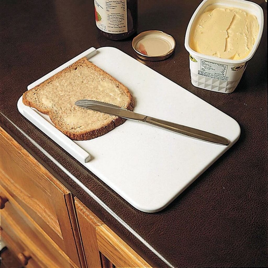 Deska kuchenna z narożnikiem na której leży kromka posmarowana masłem, a na kromce opiera się nóż