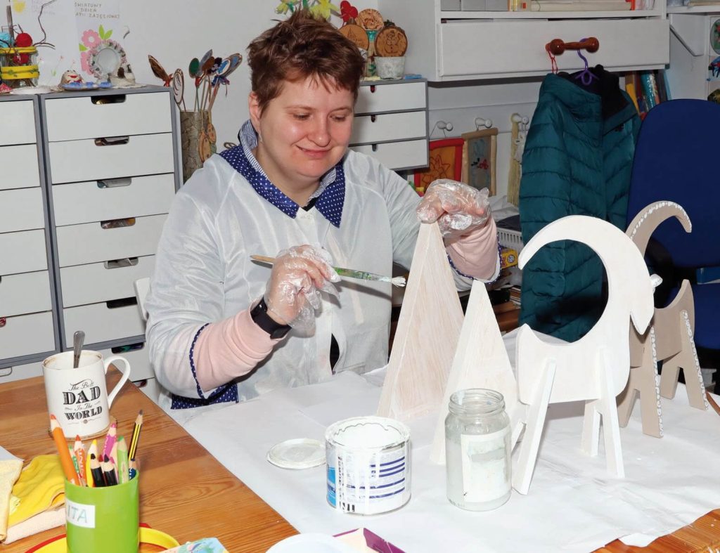 Uczestniczka Warsztatu Terapii Zajęciowej w Górkach maluje świąteczne ozdoby