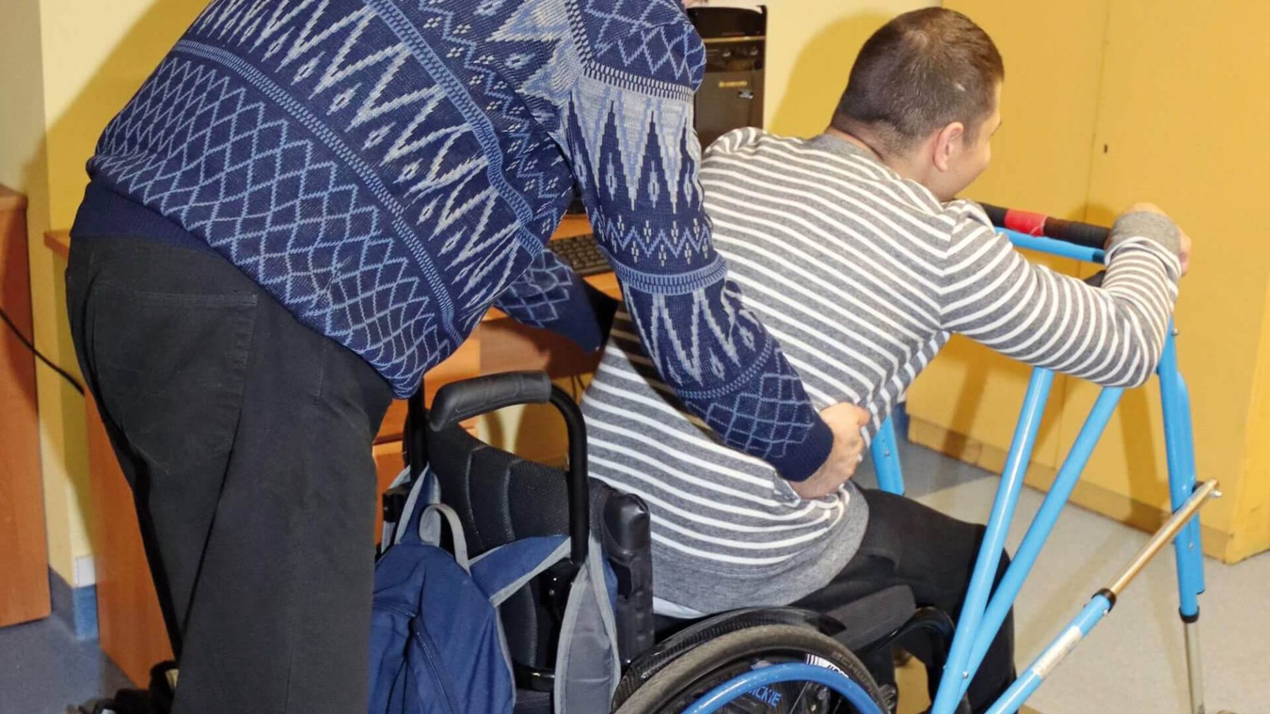 Uczestnik Warsztatu Terapii Zajęciowej w Górkach pomaga drugiemu uczestnikowi wstać z wózka inwalidzkiego