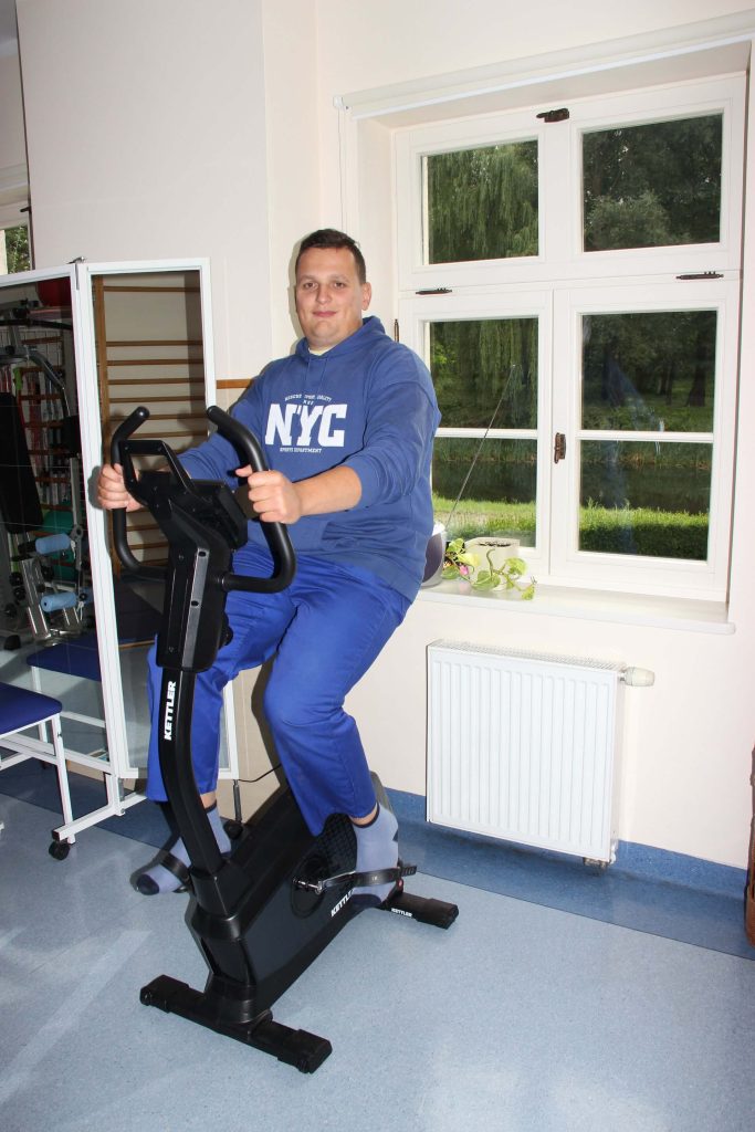 Arkadiusz Wąsik na rowerze stacjonarnym w pracowni kinezyterapii