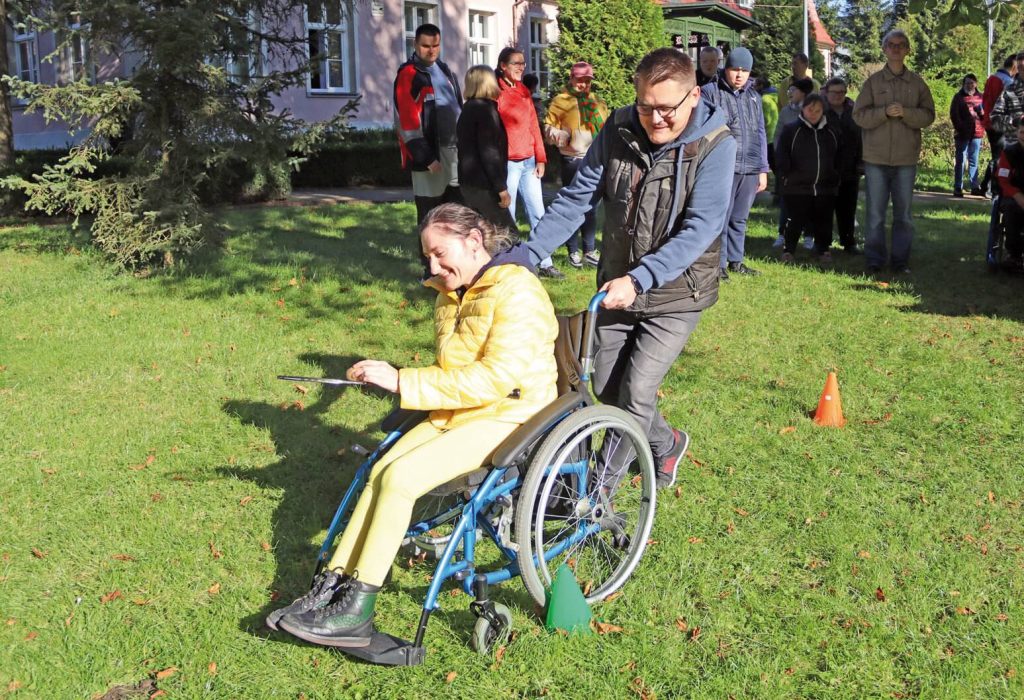 Uczestniczka Warsztatu Terapii Zajęciowej w Górkach na wózku prowadzona przez intruktora