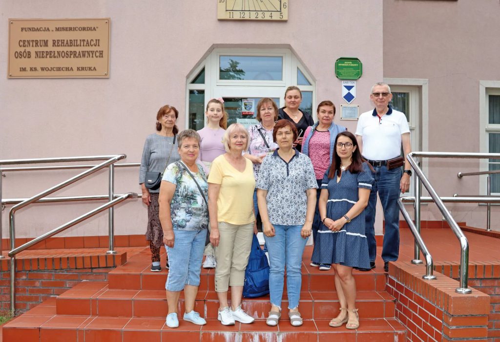Zdjęcie grupowe Ukrainek i Bogdana Muchowskiego przed siedzibą Warsztatu Terapii Zajęciowej w Górkach