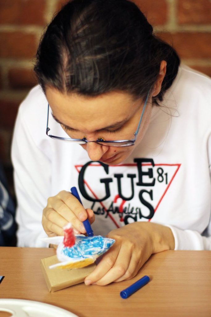 Uczestniczka Warsztatu Terapii Zajęciowej w Górkach koloruje ptaka z papieru mâché podczas zajęć w kwidzyńskim zamku