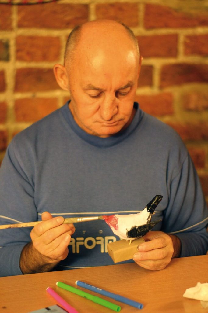 Uczestnik Warsztatu Terapii Zajęciowej w Górkach maluje ptaka z papieru mâché podczas zajęć w kwidzyńskim zamku