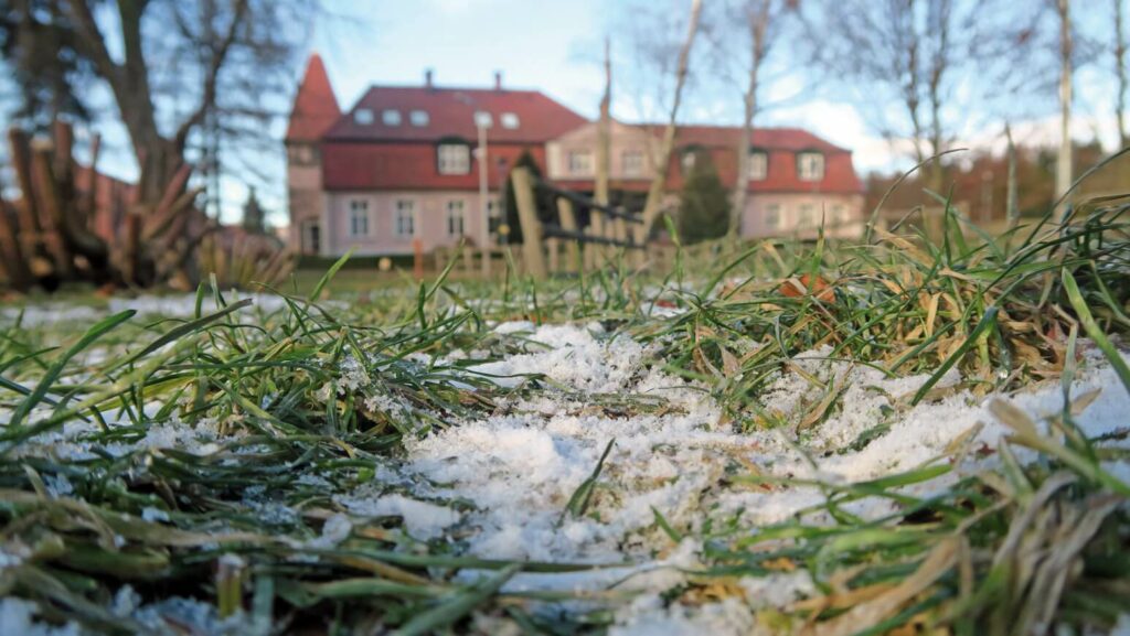 Zdjęcie konkursowe przedstawiające śnieg na trawie z siedzibą Warsztatu Terapii Zajęciowej w tle