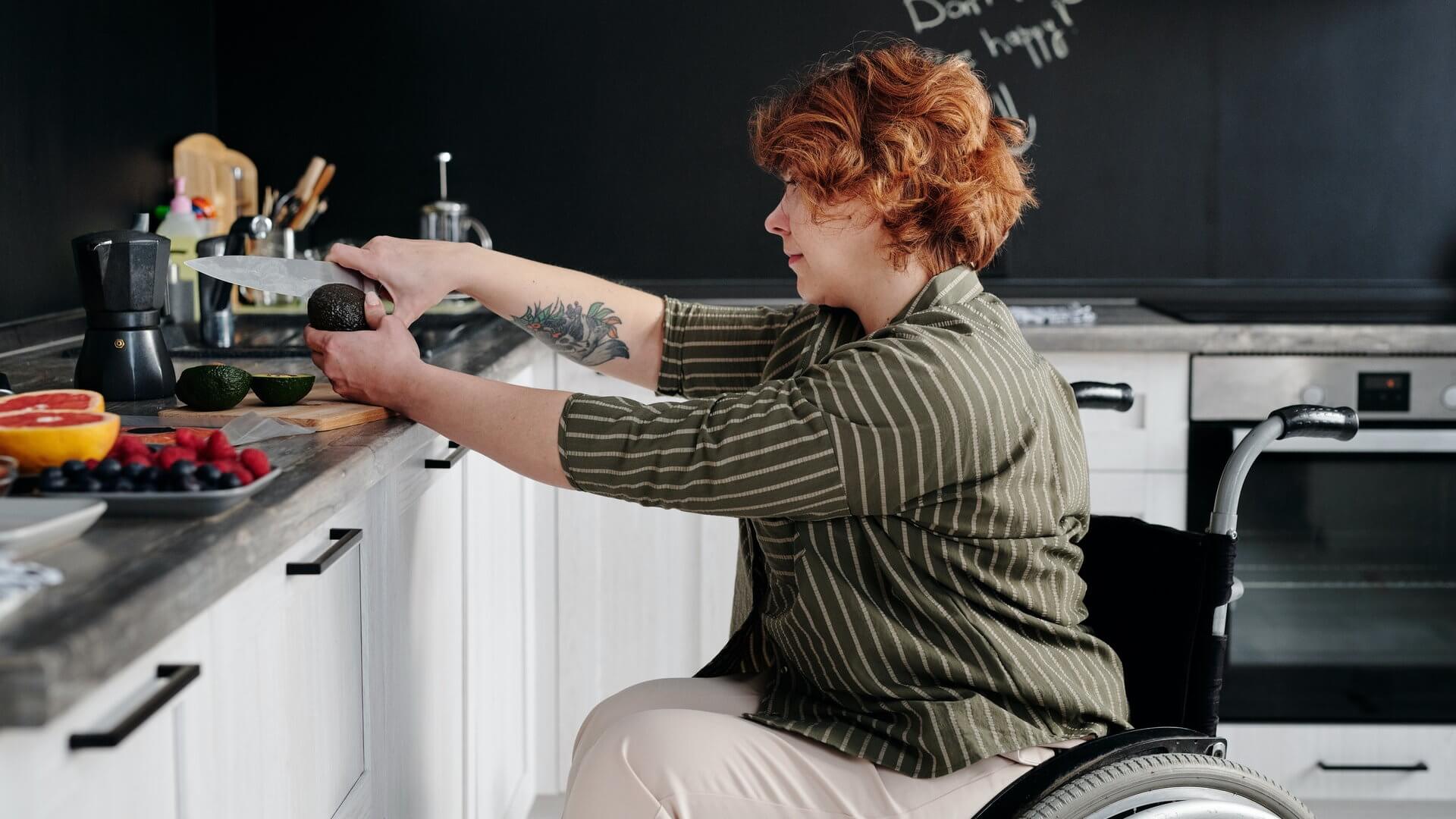 Kobieta na wózku inwalidzkim w kuchni kroi awokado